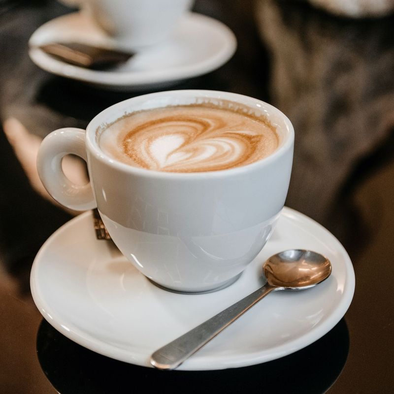 A steaming cappuccino with a latte-art heart on a white saucer
